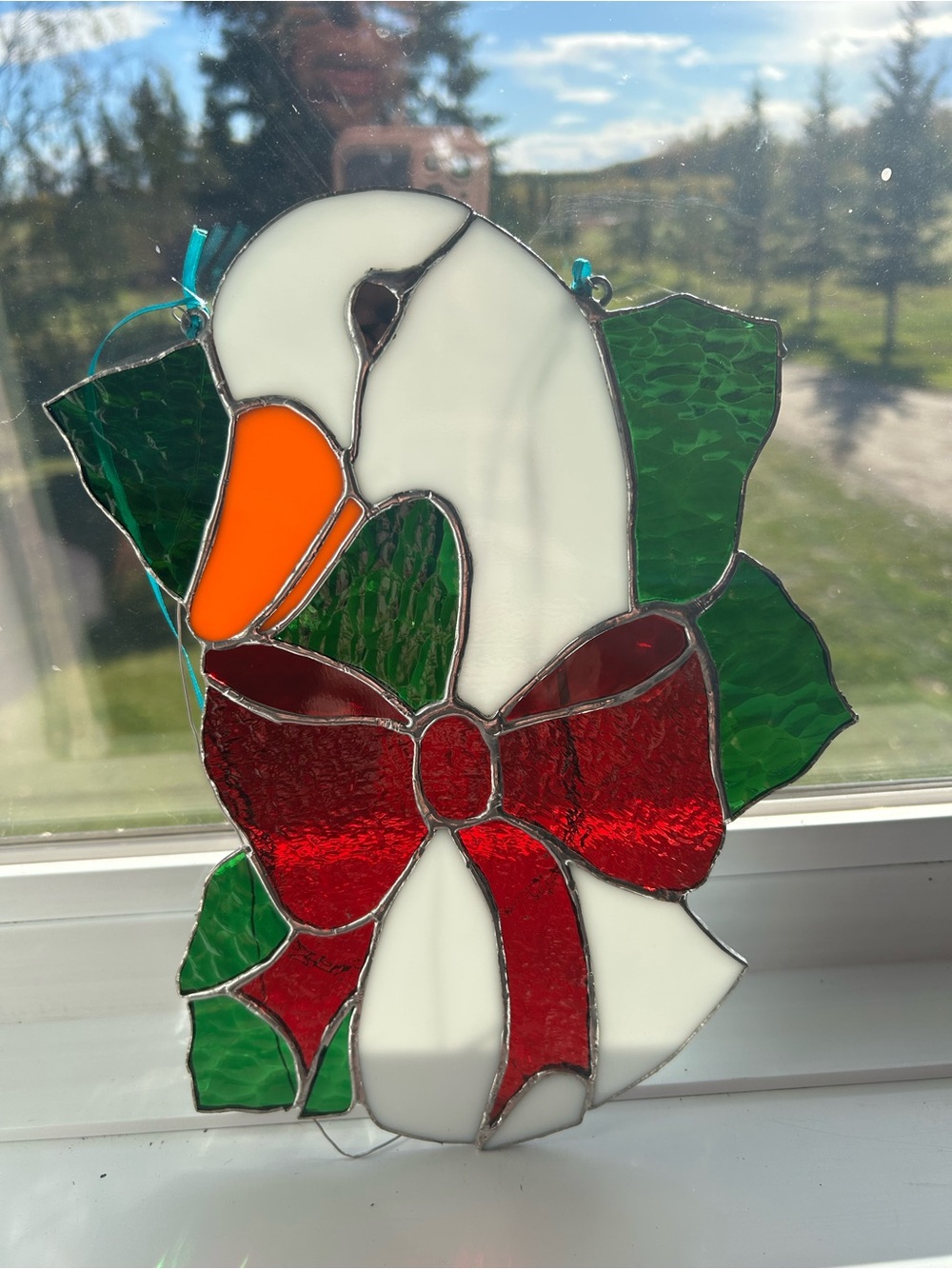 A handmade stained glass Christmas goose suncatcher with a red bow.